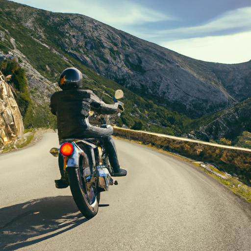 Người đàn ông mặc áo da lái xe mô tô cũ trên con đường quanh co đèo núi.